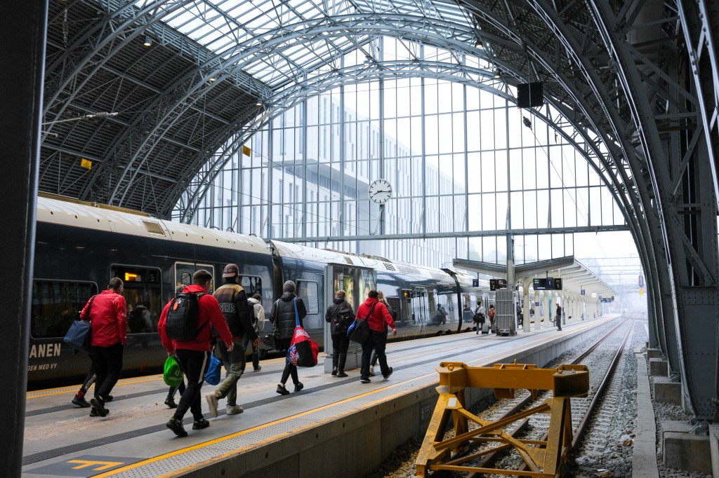 Passengers disembarking from a train at a modern railway station with a large glass roof and clock.