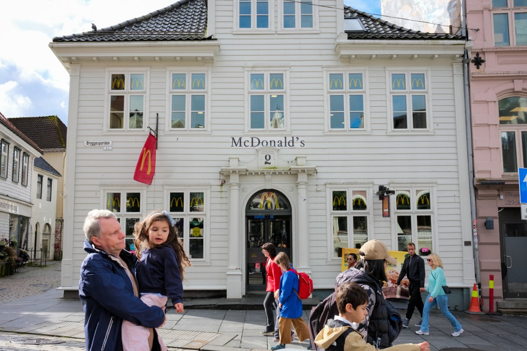 A McDonald's restaurant located in a white historic building, with people walking by, including a man carrying a child.