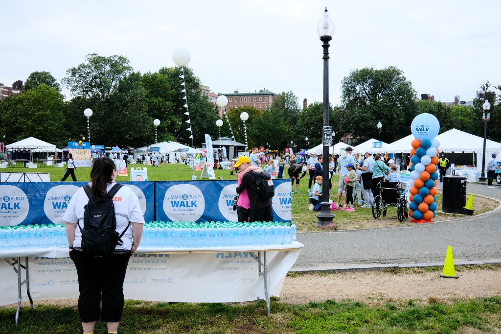 A view of a park event featuring the Jimmy Fund Walk, with tents, participants, and a table filled with water bottles.